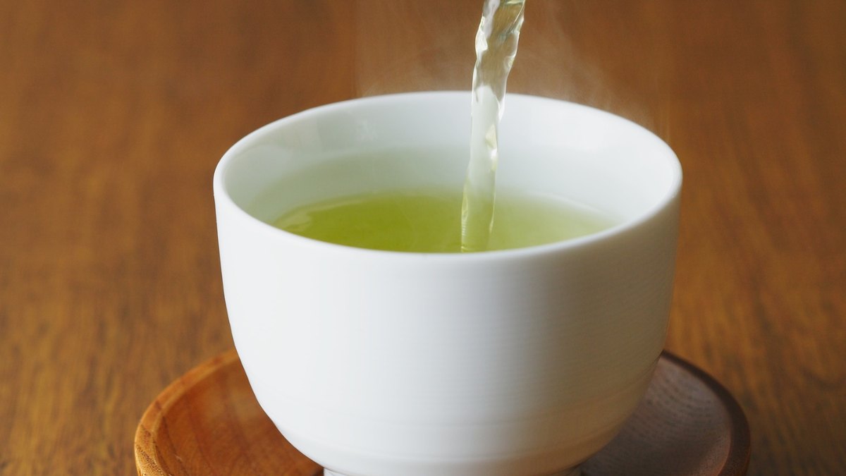 Green sencha tea being poured from a kyusu teapot into a small cup