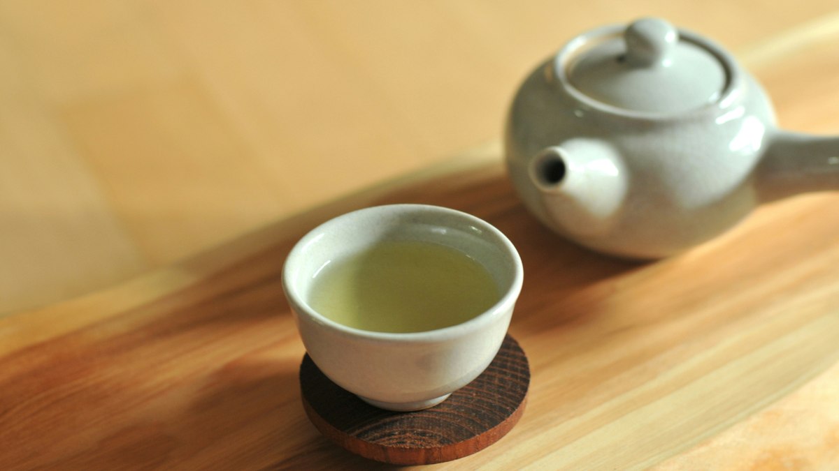 Green tea being poured slowly from a clay kyusu into a small cup