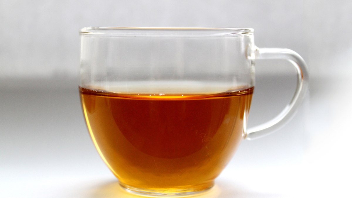 A cup of reddish-brown hojicha roasted green tea beside loose roasted leaves