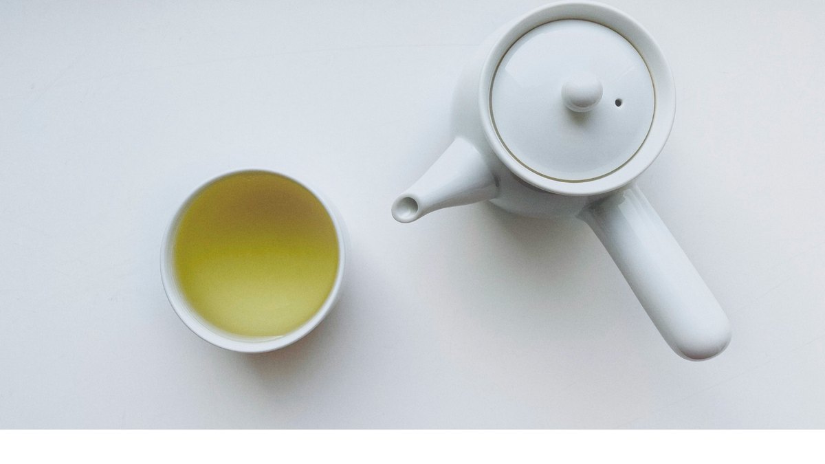 A Japanese side-handle kyusu teapot pouring green tea into a cup