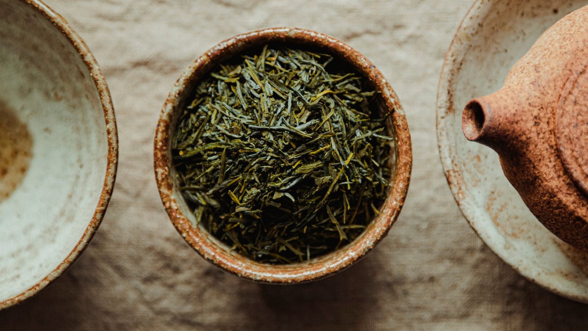 Powdered green tea in a spoon beside loose green tea leaves