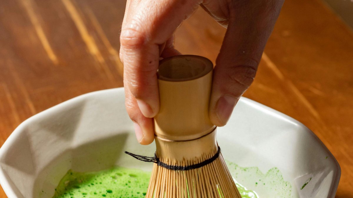 A matcha bowl, bamboo whisk and scoop arranged on a wooden surface