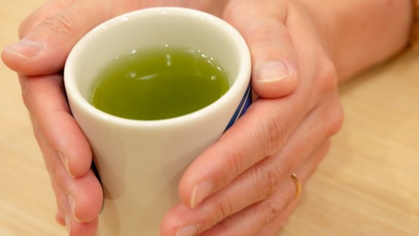 Two hands cupping a Japanese yunomi of green tea