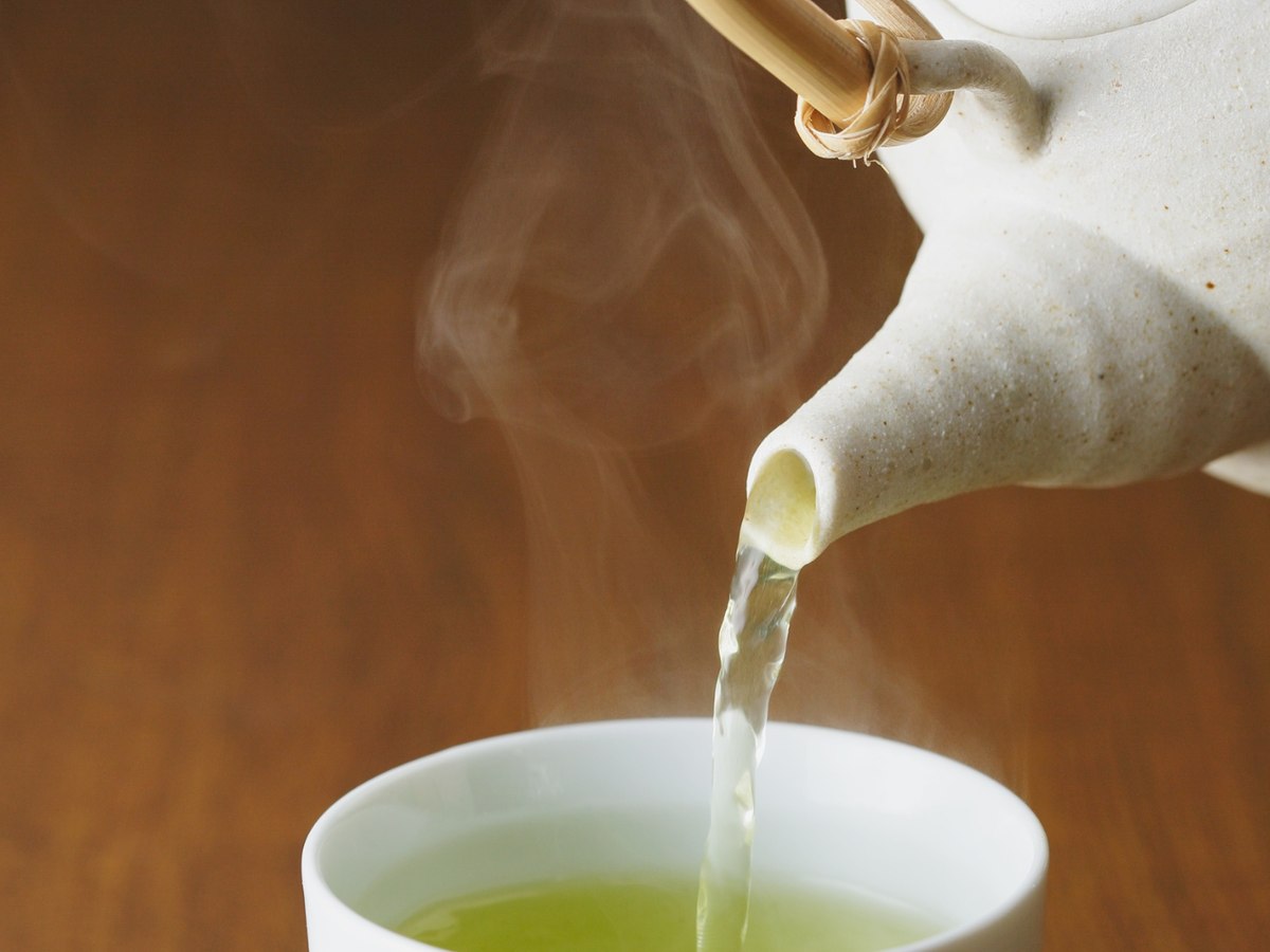 Green tea poured into a cup with steam rising