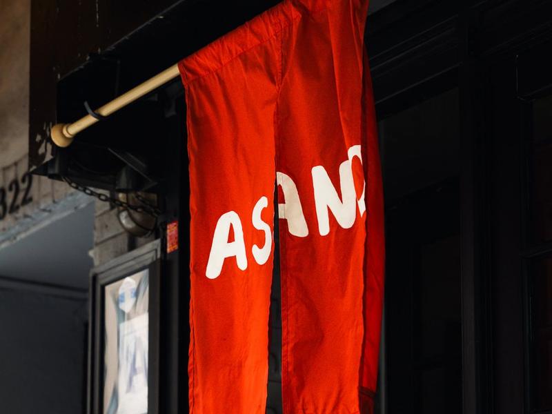The orange ASANO noren hanging from a wooden pole